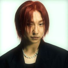 a man with red hair wearing a black jacket and silver beaded necklace on his neck