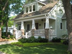 a white house with porches and pillars on the front lawn, surrounded by trees