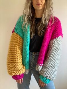 a woman standing in front of a white wall wearing a multicolored cardigan