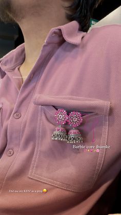 a close up of a person wearing a pink shirt with two earrings in the pocket