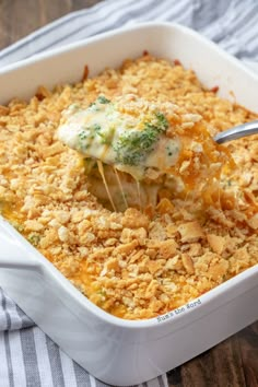 a casserole dish with broccoli and cheese being scooped from the casserole