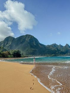 a person standing on the beach with their feet in the water and mountains in the background