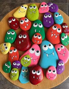 colorful rocks with faces painted on them sitting on a wooden plate in front of a tile floor