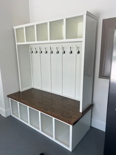 a white bench with several coats on it in the corner of a room next to a refrigerator