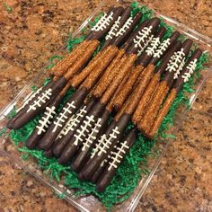 chocolate football pretzels are arranged on top of green grass in a clear tray