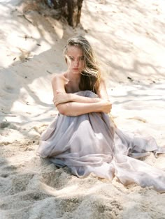 a woman sitting in the sand with her arms crossed