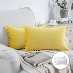 two yellow pillows sitting on top of a white couch next to a magazine and potted plant