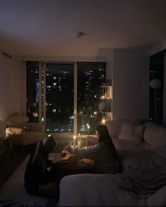 two people sitting on a couch in a living room with the city lights lit up