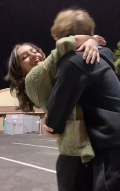 a woman holding a child in her arms while standing on top of a parking lot