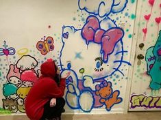 a person sitting on the ground in front of a wall with hello kitty pictures painted on it