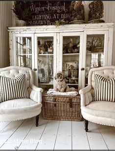 two chairs and a cabinet with a dog sitting on it in front of some plants