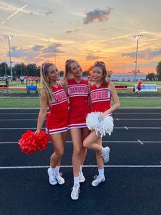 three girls in cheerleader outfits standing on a track