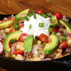 a skillet filled with chicken, avocado, tomatoes, onions and sour cream