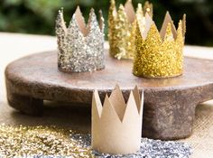 four crowns sitting on top of a wooden table next to glitter covered rocks and trees