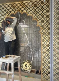 a man standing on top of a step stool in front of a wall with an intricate design