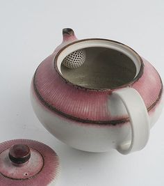 a pink and white ceramic tea pot next to a cup with a strainer on it