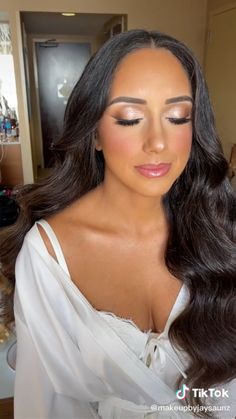 a woman with long dark hair wearing a white dress and makeup looks down at her face