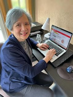 an older woman sitting at a desk using a laptop computer