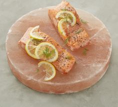 two pieces of salmon with lemons and dill on a round stone platter