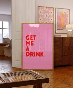 a pink poster with the words get me a drink on it in front of a wooden table