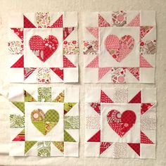 four quilt blocks with hearts on them sitting on a table next to a wall hanging