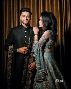 a man and woman standing next to each other in front of a curtain with gold curtains