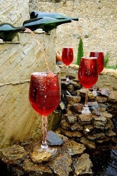 three wine glasses are being filled with red liquid from a faucet that is running down the side of a stone wall