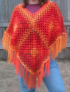 a woman wearing a red and orange crocheted ponchy with fringes