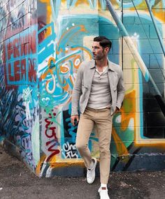 a man standing in front of a wall with graffiti on it and wearing white shoes