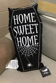 a black pillow with the words home sweet home on it sitting on a couch next to a tag