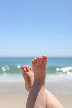 a person laying down on the beach with their feet in the sand and water behind them