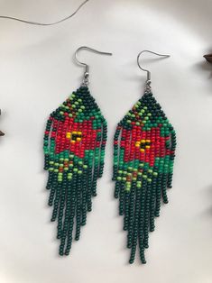 a pair of green and red beaded earrings sitting on top of a white surface