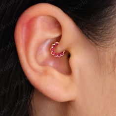 a woman's ear with a small red heart shaped nose ring on top of it