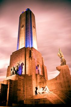 a very tall tower with some statues on it's sides and lights on at the top