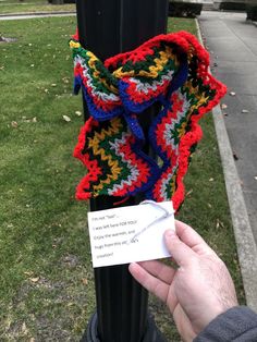 someone is holding up a crocheted scarf on a pole