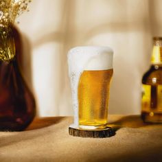 a glass of beer sitting on top of a wooden table next to two vases