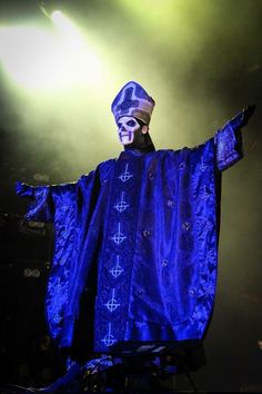 a man dressed in blue is standing on stage with his arms out and hands outstretched