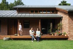 three people sitting on the front porch of a brick house with solar panels on the roof