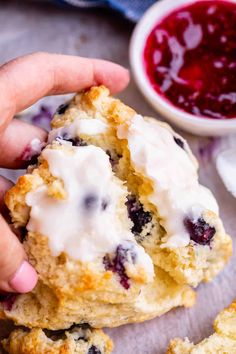 a person holding a blueberry scones with white icing on it and some cranberry sauce in the background