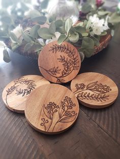 four wooden coasters sitting on top of a table next to flowers and greenery