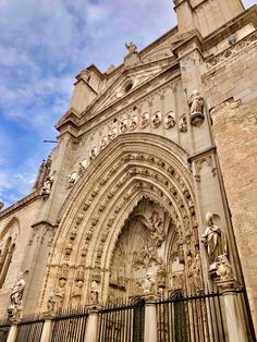 an old cathedral with statues on the front and side walls, against a cloudy blue sky