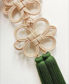 two tassels are attached to a wall hanging on a white wall, one has a green tassel and the other is made out of rope