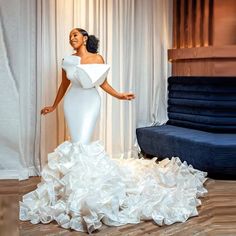 a woman standing in front of a couch wearing a white dress with ruffles on it