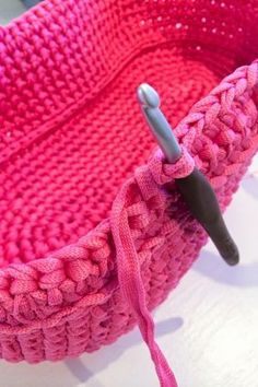 a pink crocheted basket with a hook in the middle and a button on it