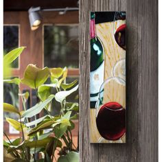 a wine bottle and glass hanging on the side of a wooden wall next to a potted plant