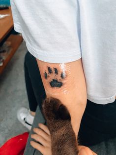 a person with a cat paw tattoo on their left arm and the other hand is holding an animal's paw