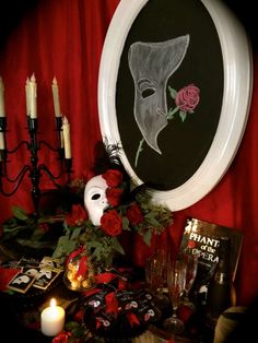 a table topped with candles and pictures next to a wall mounted mask on the wall