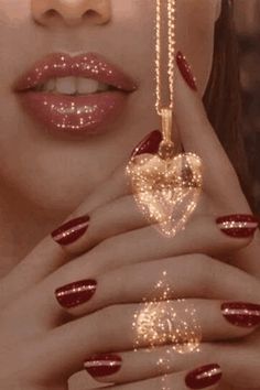 a woman with red and gold nail polish holding a heart shaped object in her hands