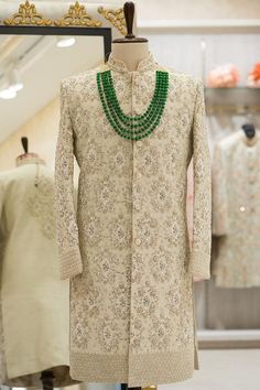 a mannequin with green beads on it in front of clothing racks and dresses