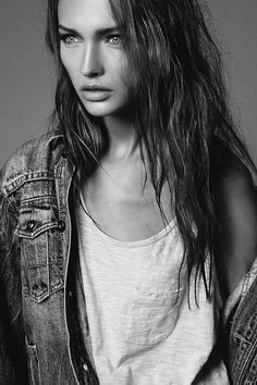 a black and white photo of a woman with long hair wearing a jean jacket, looking at the camera